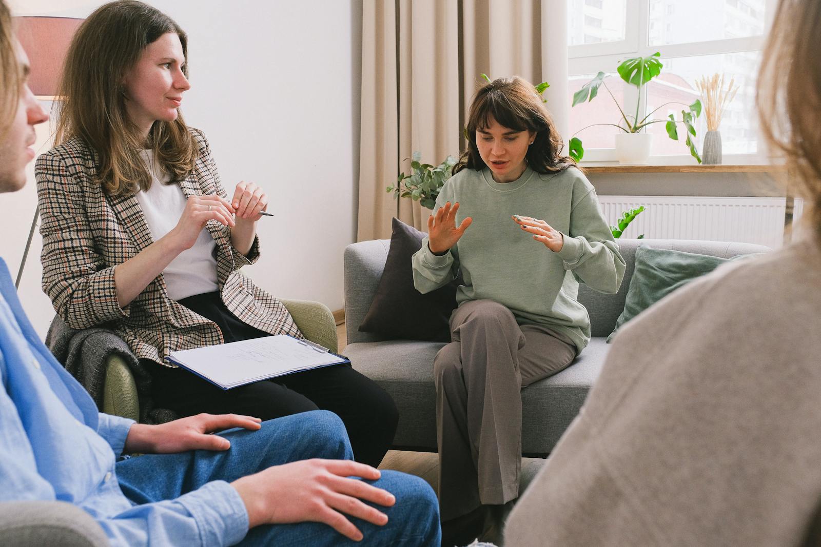 A small group seated together in a warm therapy office — peer consultation with soft natural light, plants by the window, and a comfortable couch